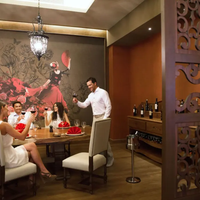 Friends enjoying wine at a stylish restaurant with ornate chandeliers and a large wall mural.