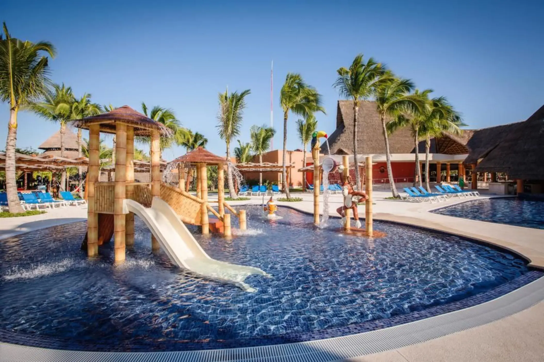 A vibrant kids' pool area with multiple water slides, shallow play areas, and palm trees.