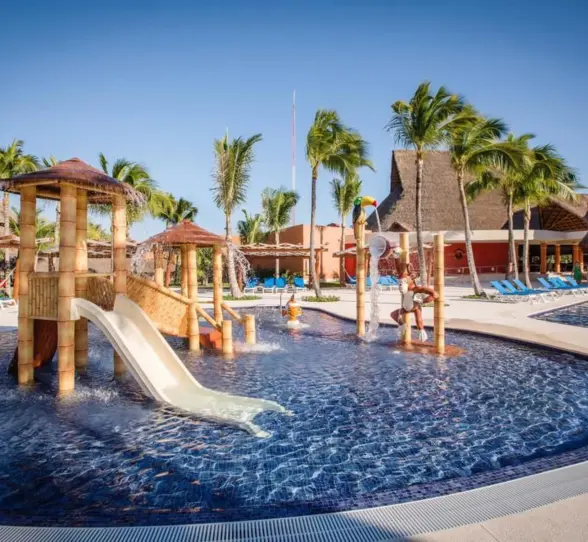 A vibrant kids' pool area with multiple water slides, shallow play areas, and palm trees.