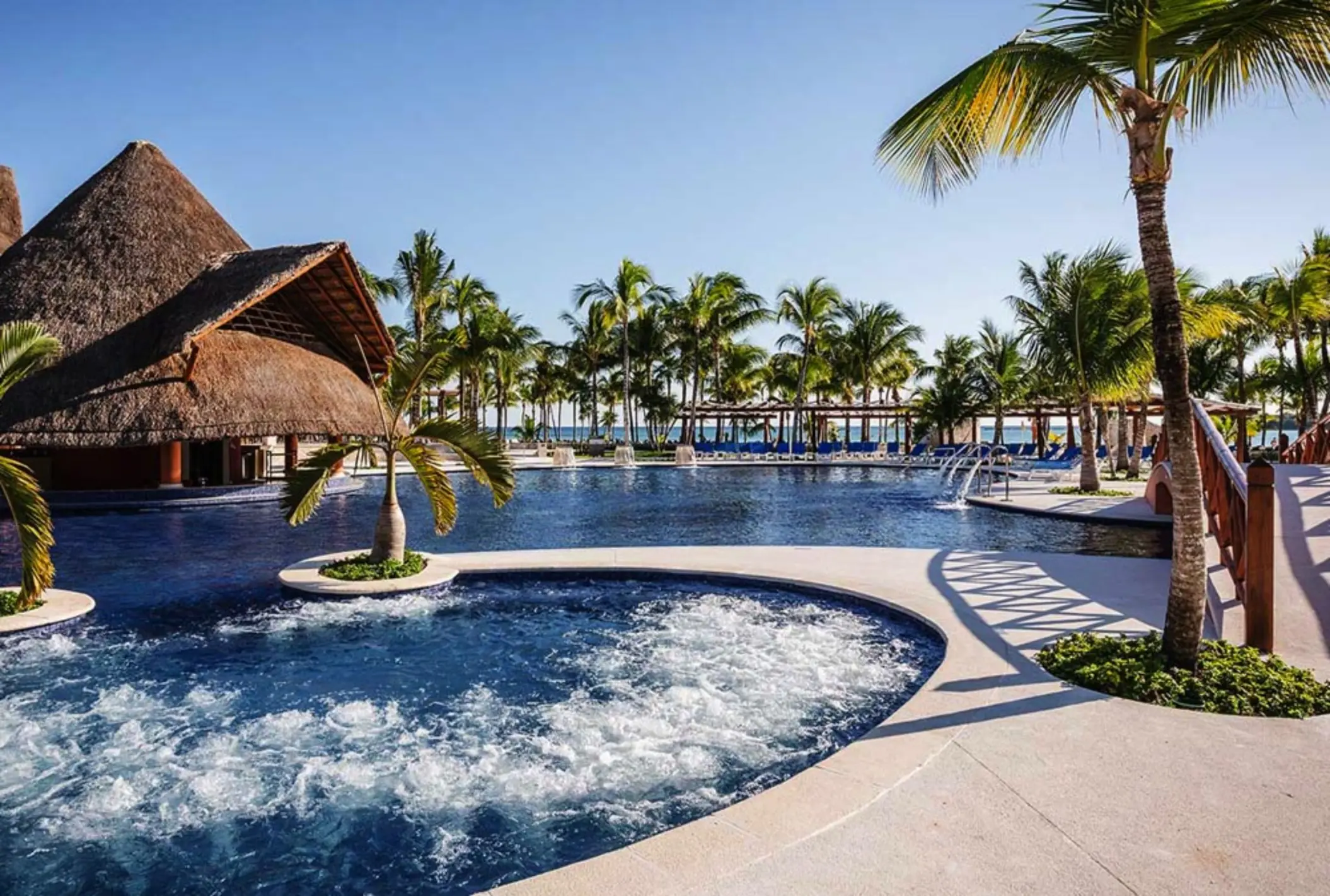 A large, inviting resort pool with a swim-up bar, surrounded by lush palm trees and cabanas.
