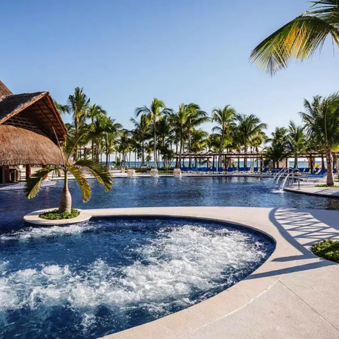 A large, inviting resort pool with a swim-up bar, surrounded by lush palm trees and cabanas.