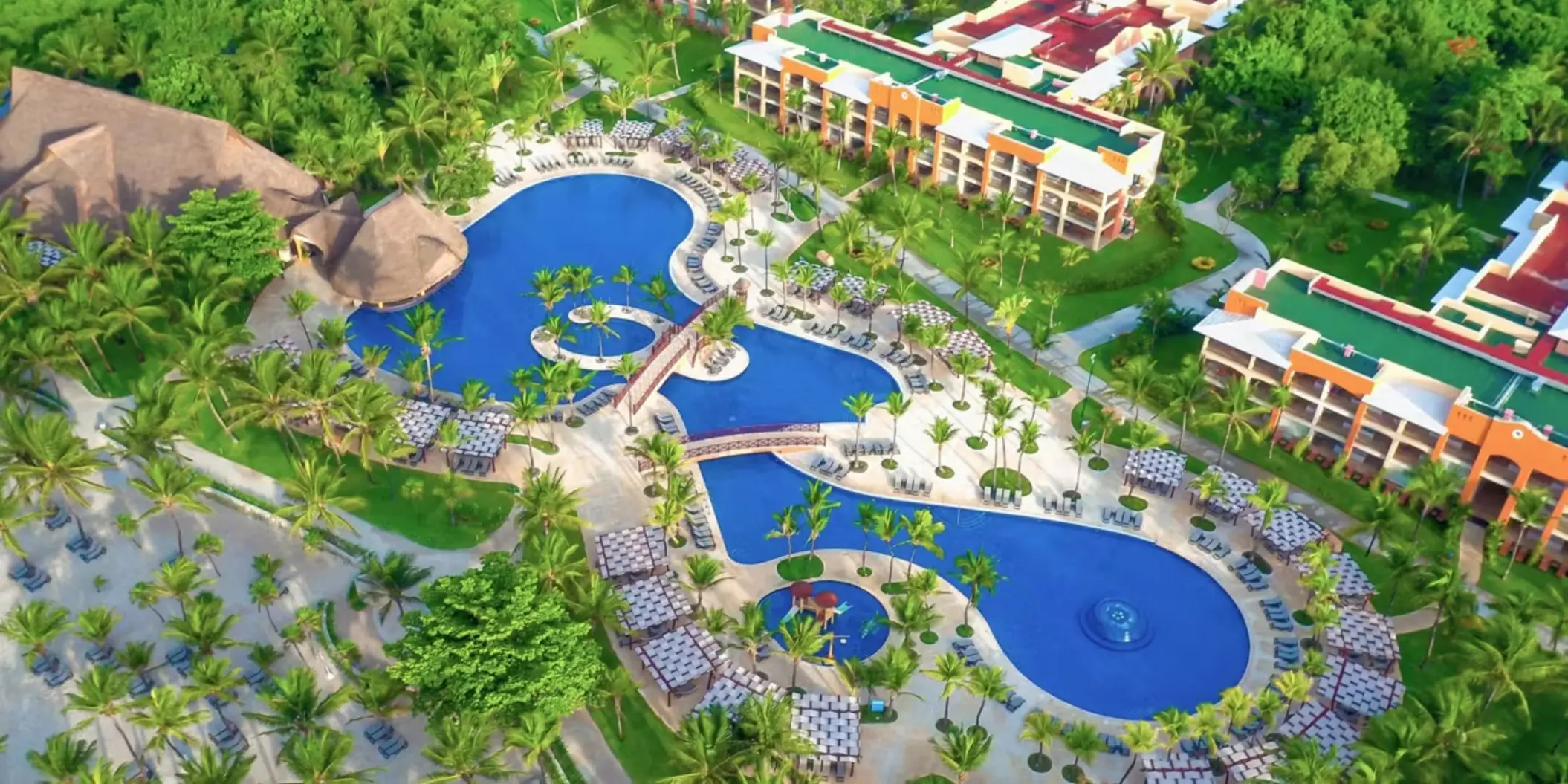 An aerial view showing the large, free-form swimming pools surrounded by palm trees and buildings.