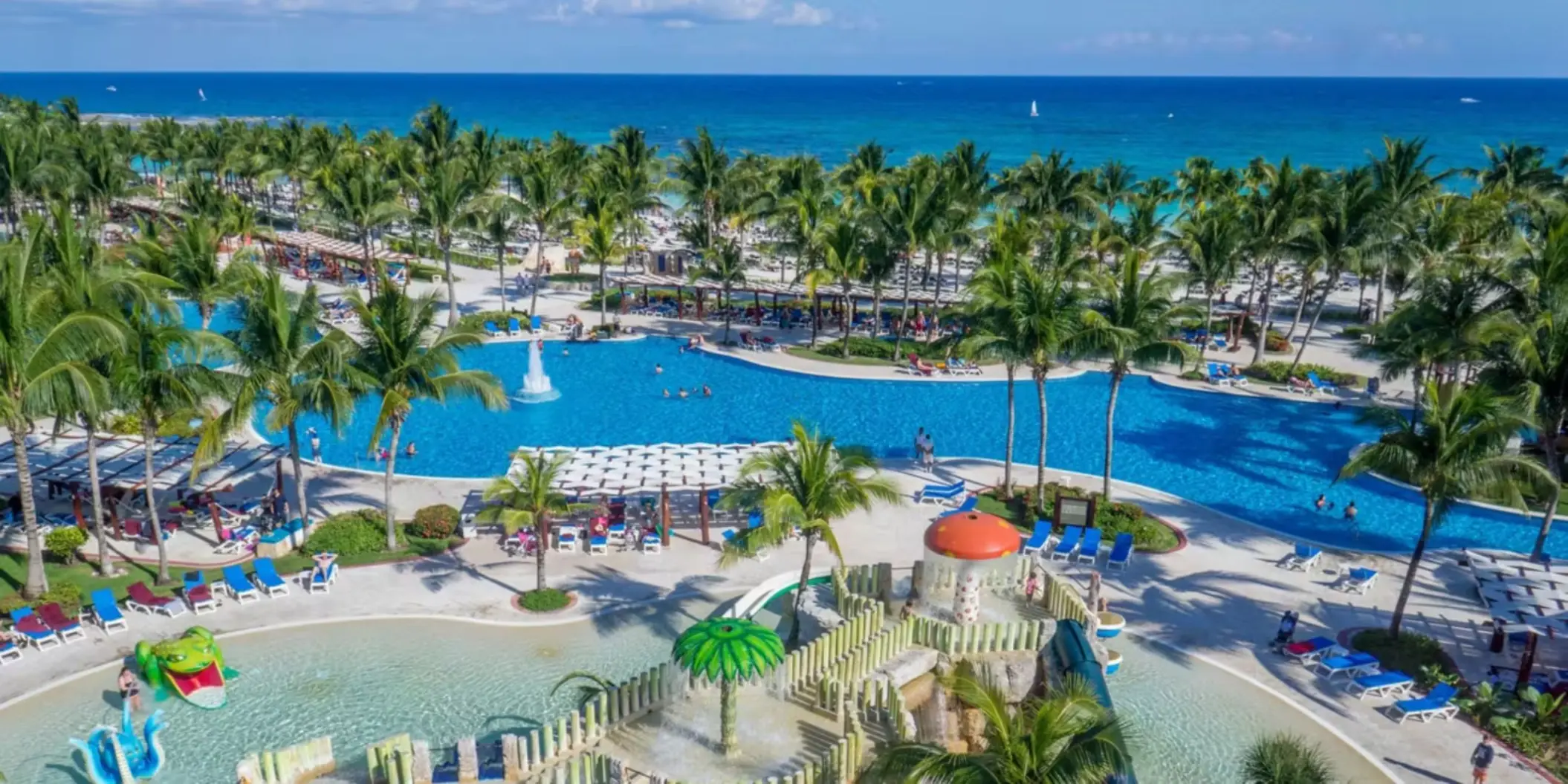 An aerial view of the resort with its large pools, kids' water park, and the beach in the background.