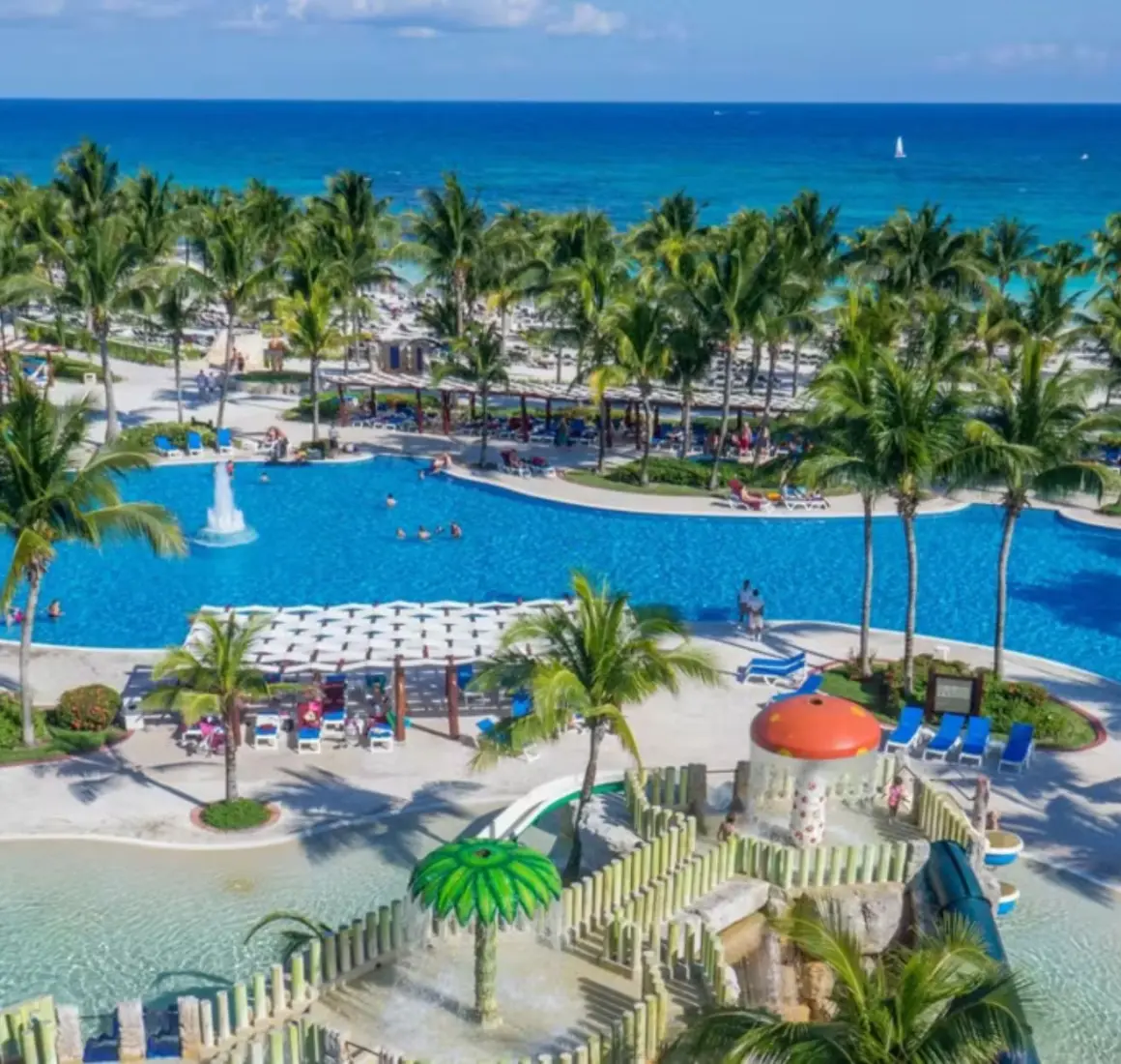 An aerial view of the resort with its large pools, kids' water park, and the beach in the background.