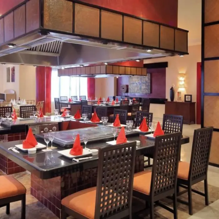 The interior of an elegant Asian restaurant with a teppanyaki grill station and neatly set tables.