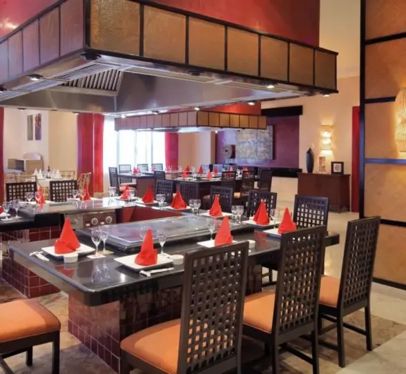 The interior of an elegant Asian restaurant with a teppanyaki grill station and neatly set tables.