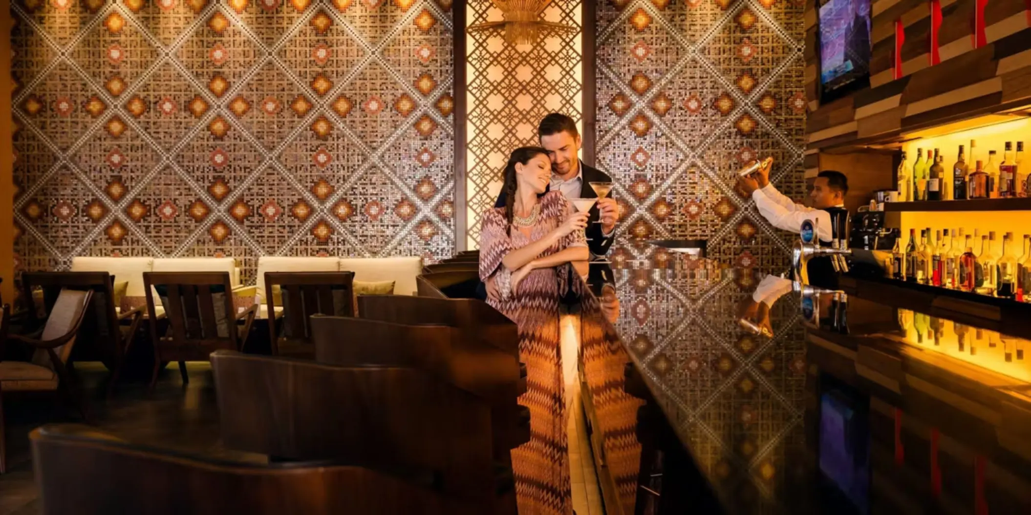 A young couple at a stylish bar, enjoying drinks while a bartender prepares a cocktail for them.