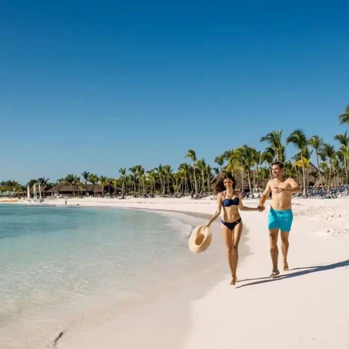 A happy couple holding hands and running along the stunning white sand beach next to the turquoise sea.