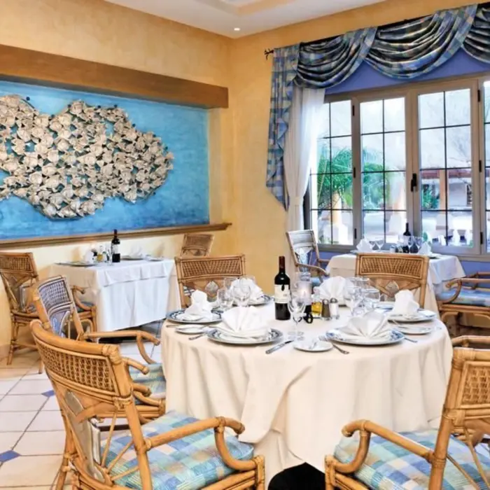 A fine dining restaurant with a nautical theme, featuring a large sea-inspired art piece and woven chairs.
