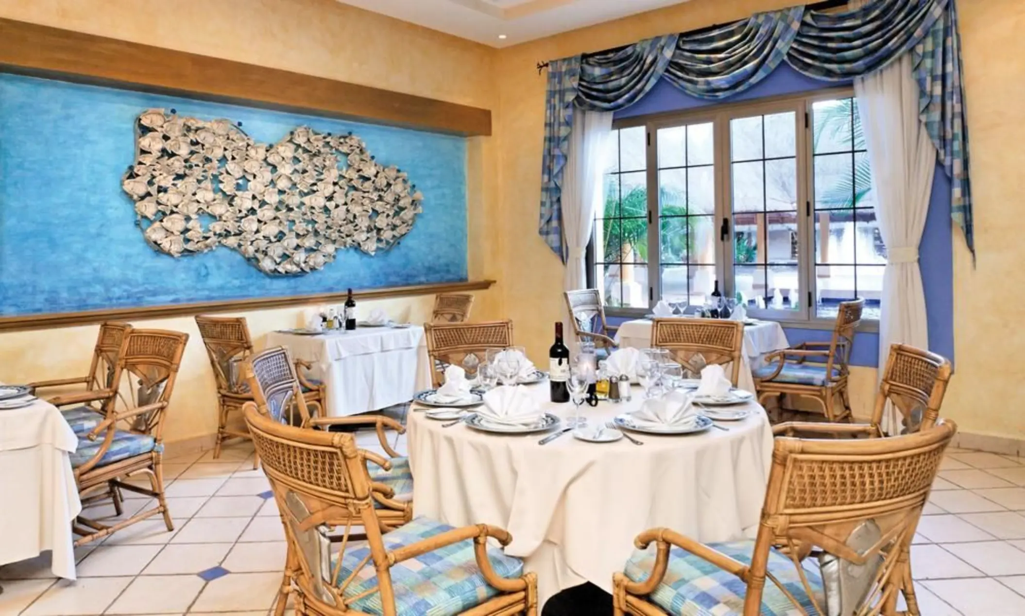 A fine dining restaurant with a nautical theme, featuring a large sea-inspired art piece and woven chairs.