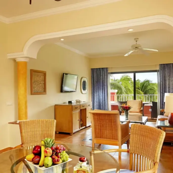 A spacious hotel suite with a living area, a dining table, and a separate bedroom visible through an archway.