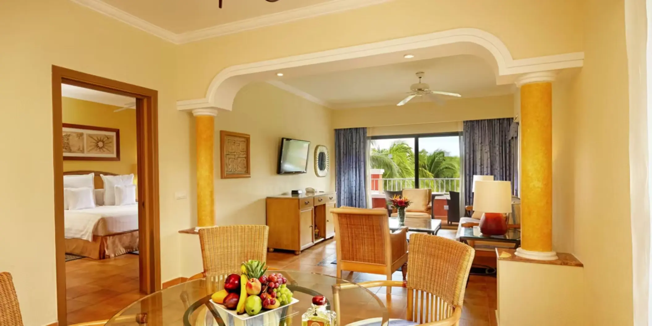 A spacious hotel suite with a living area, a dining table, and a separate bedroom visible through an archway.