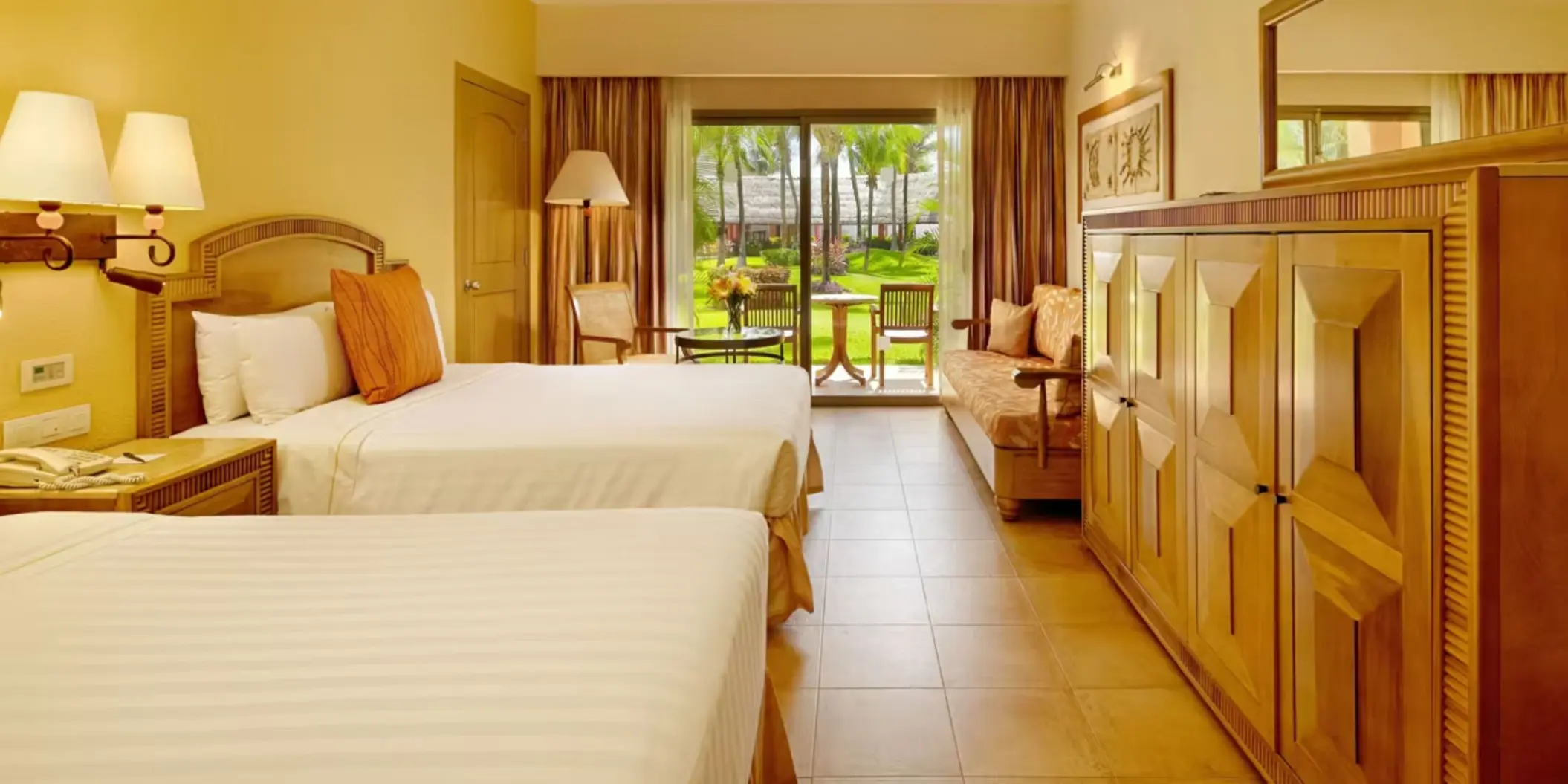A hotel suite with two double beds, a sofa, and a patio with a table and chairs.