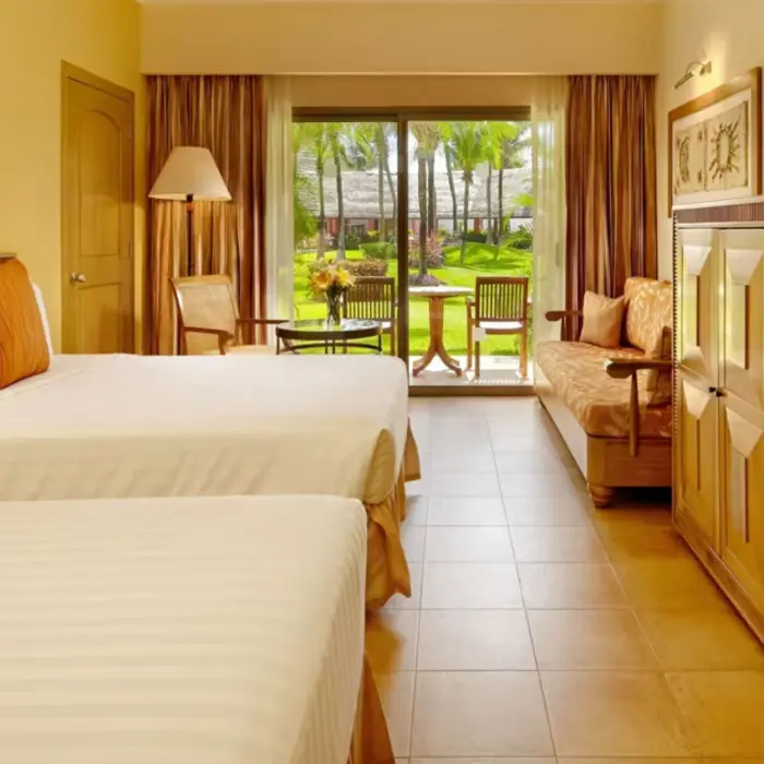 A hotel suite with two double beds, a sofa, and a patio with a table and chairs.