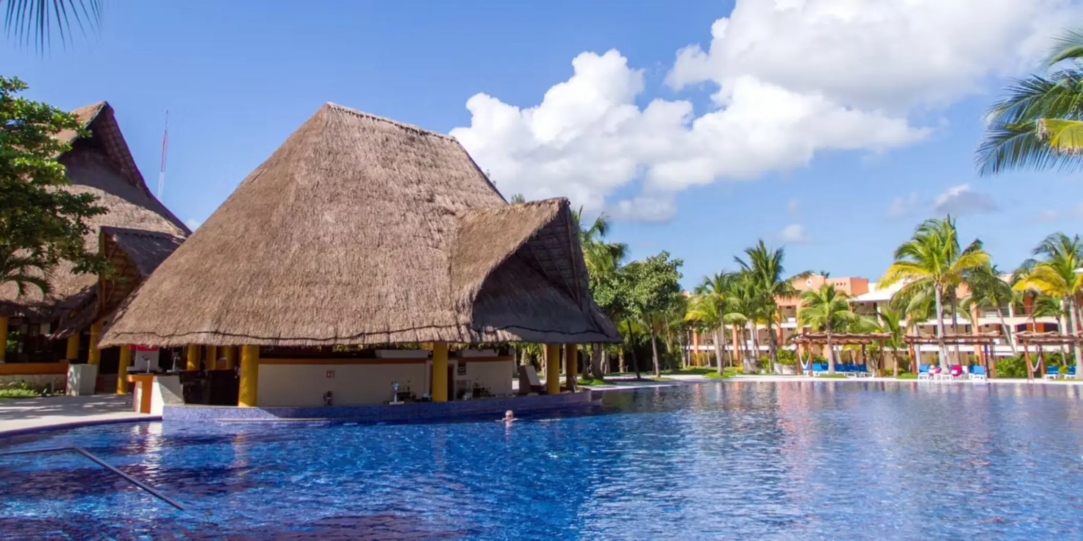 A rustic thatched-roof swim-up bar located in the middle of a large, inviting swimming pool.