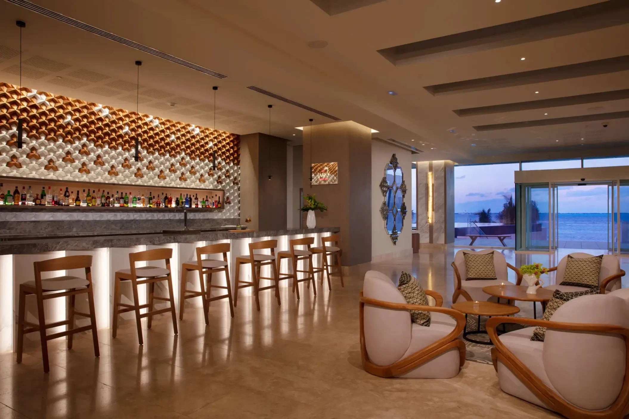 Chic indoor bar with sleek wooden seating and stylish decor, offering ocean views through glass doors.
