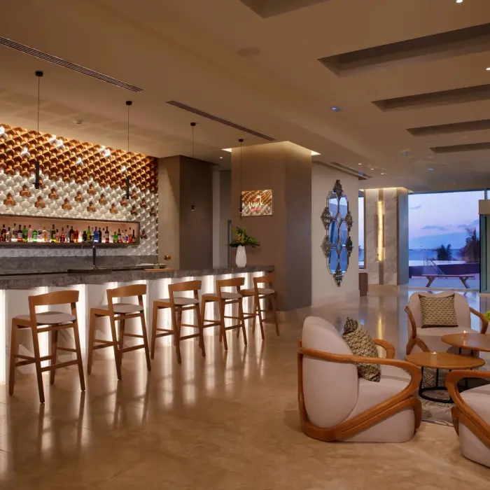 Chic indoor bar with sleek wooden seating and stylish decor, offering ocean views through glass doors.