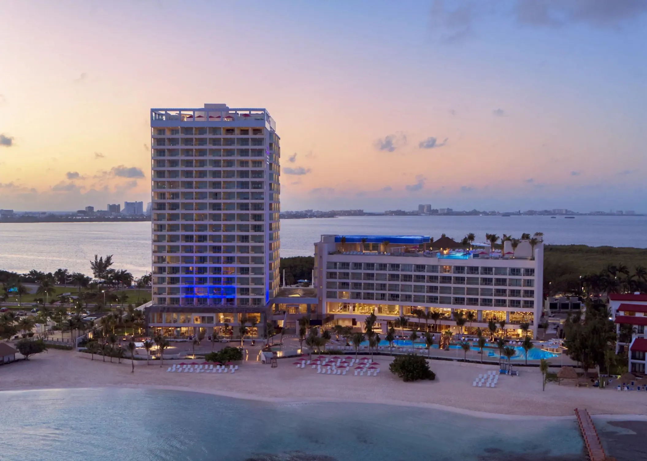 Nighttime aerial view of Breathless Cancun Soul Resort with lit-up buildings and calm ocean surroundings.