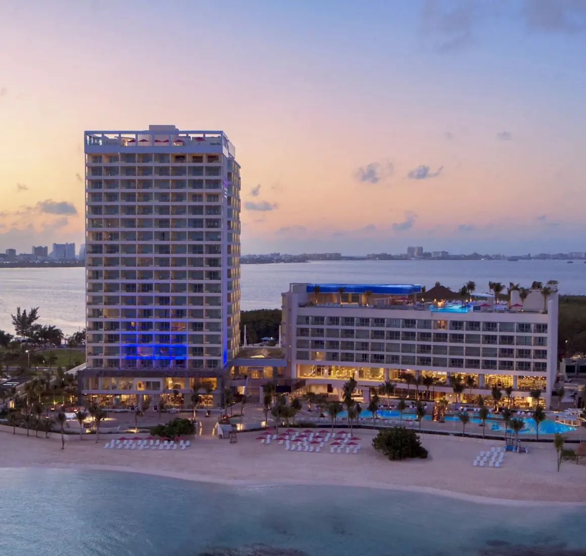 Nighttime aerial view of Breathless Cancun Soul Resort with lit-up buildings and calm ocean surroundings.