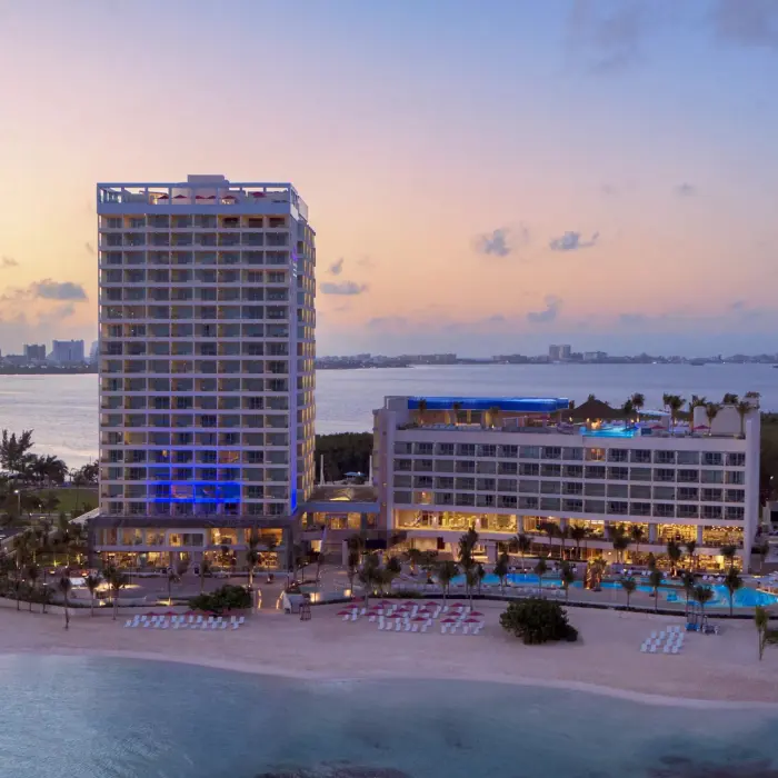 Nighttime aerial view of Breathless Cancun Soul Resort with lit-up buildings and calm ocean surroundings.