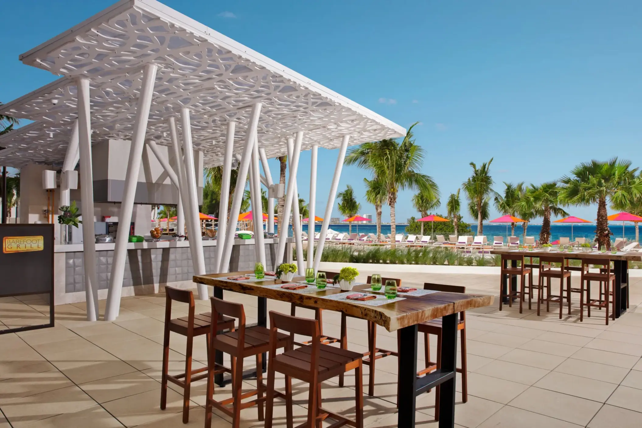 Casual outdoor setup at Barefoot Grill near the pool area with palm trees and colorful umbrellas.