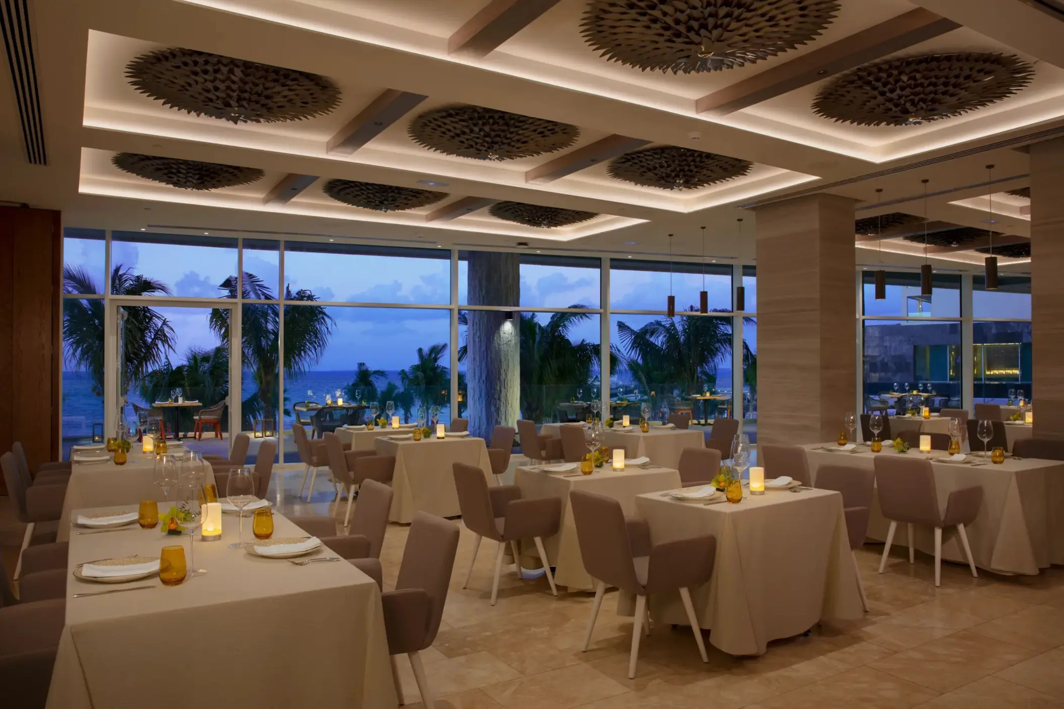 Elegant indoor dining setup at Kibbeh restaurant with ocean views and soft evening lighting.