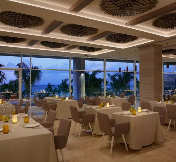 Elegant indoor dining setup at Kibbeh restaurant with ocean views and soft evening lighting.