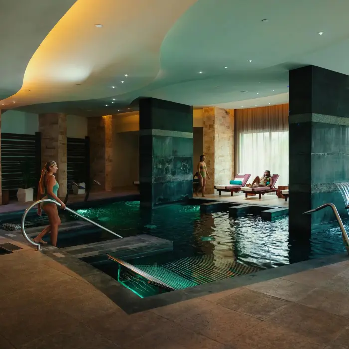 Indoor spa hydrotherapy pool with cascading waterfalls, mood lighting, and wellness ambiance.