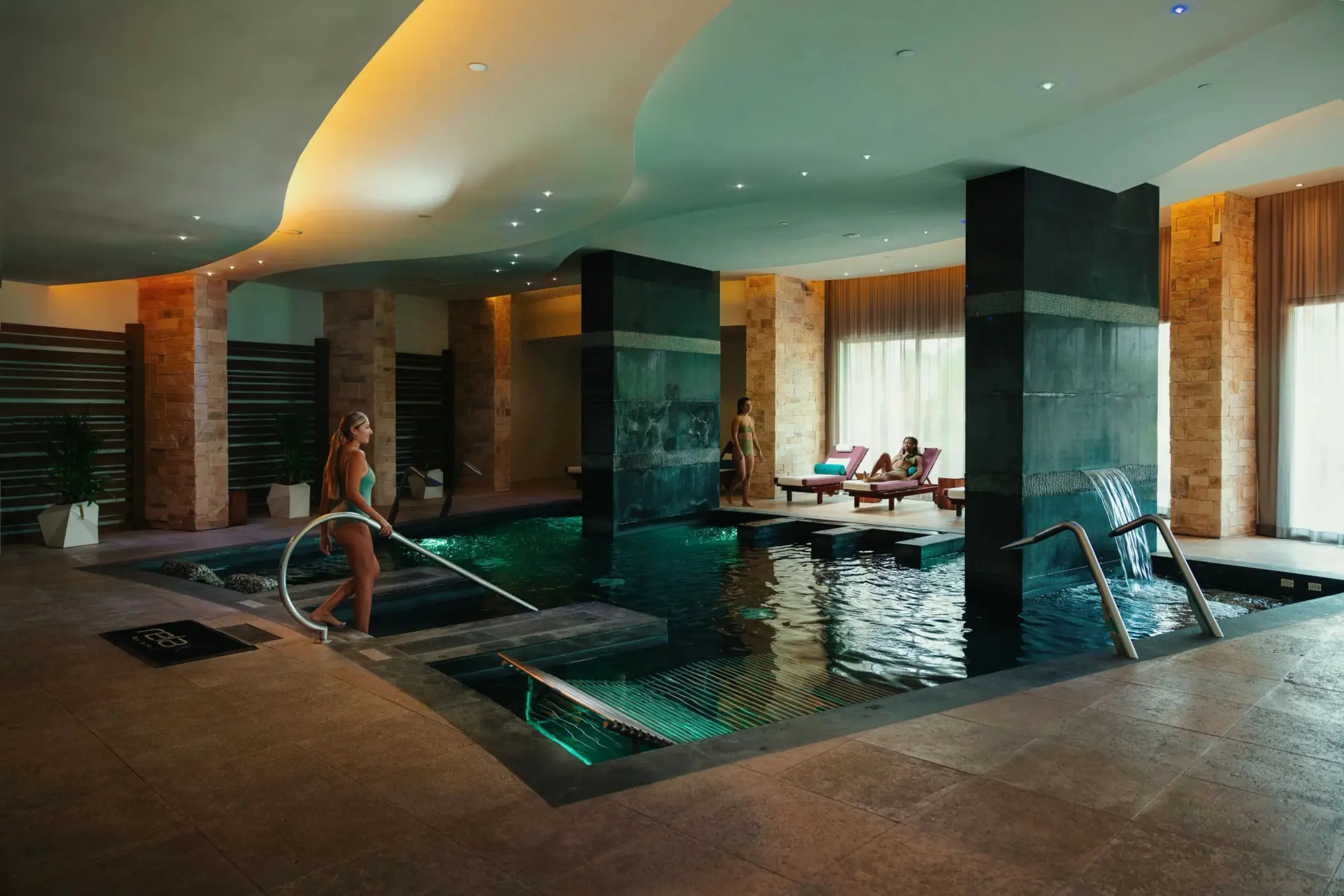 Indoor spa hydrotherapy pool with cascading waterfalls, mood lighting, and wellness ambiance.