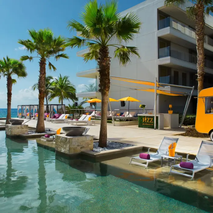 Bright yellow Veuve Clicquot cart and champagne bar beside sunny beachfront pool.
