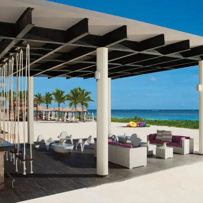 Swing-seat beach bar with lounge furniture overlooking white sand and turquoise ocean.