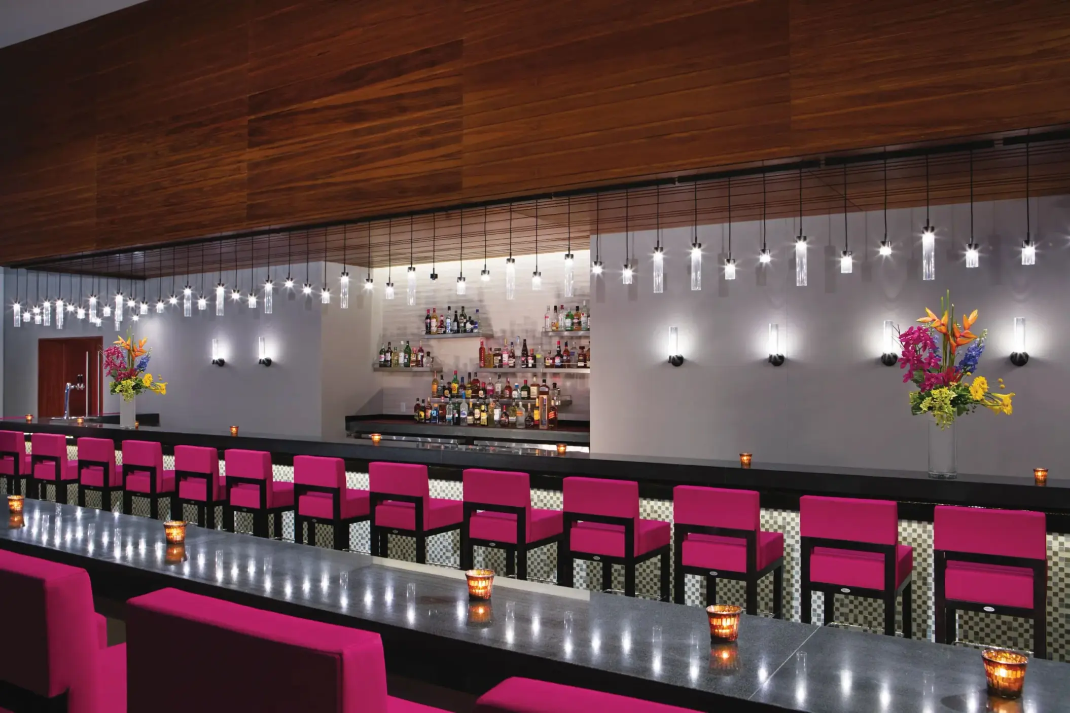 Sleek modern lobby bar with pink chairs, pendant lights, and a fully stocked back bar.