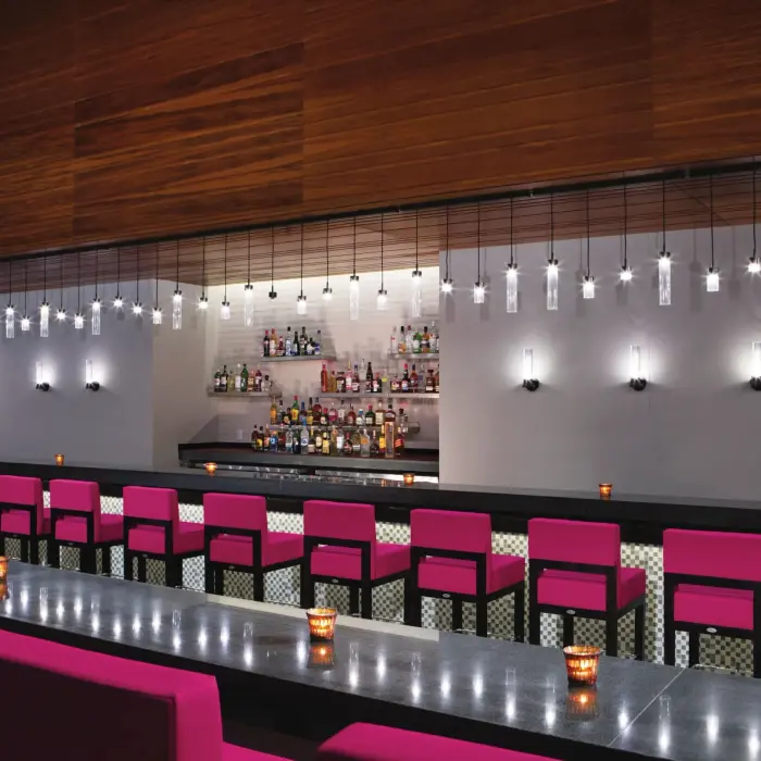 Sleek modern lobby bar with pink chairs, pendant lights, and a fully stocked back bar.