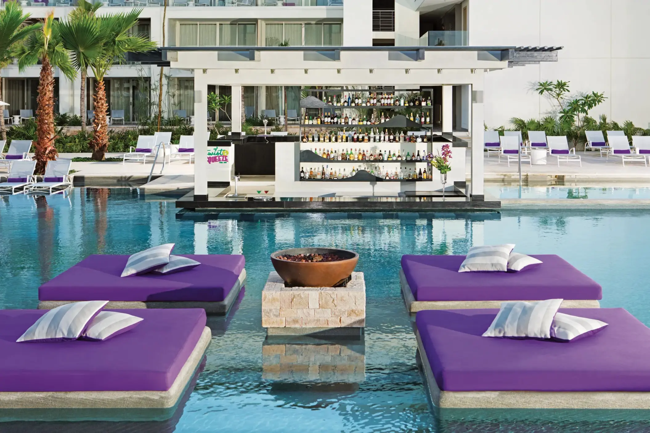Colorful pool bar with floating purple loungers and views of the resort buildings.