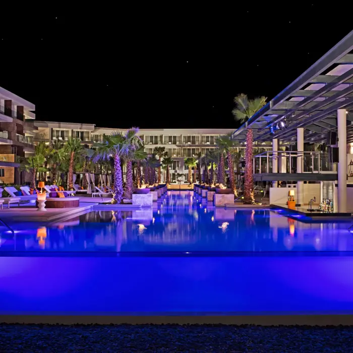 Freestyle pool at night with glowing fire pits and palm trees at Breathless Riviera Cancun’s vibrant pool deck.
