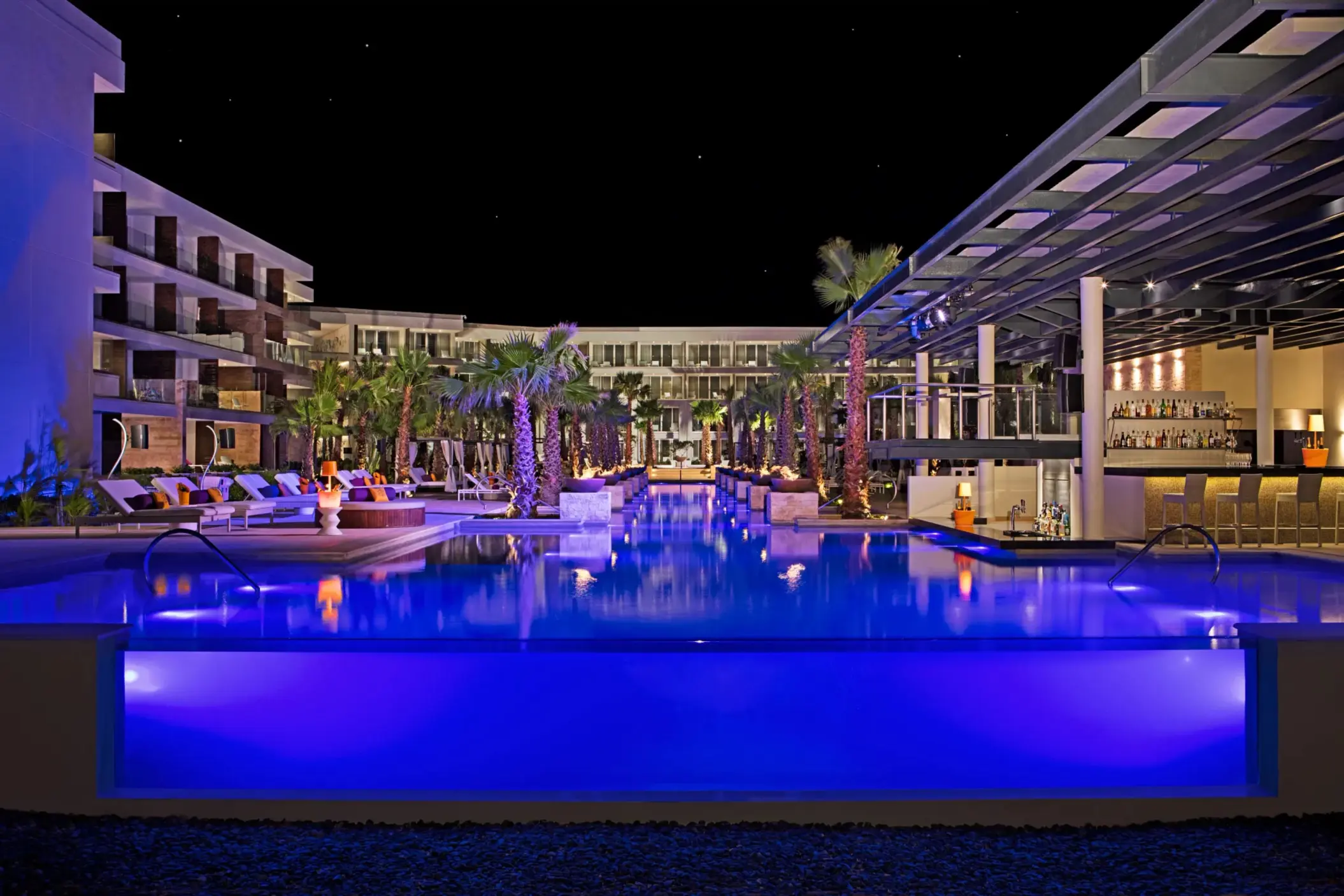 Freestyle pool at night with glowing fire pits and palm trees at Breathless Riviera Cancun’s vibrant pool deck.