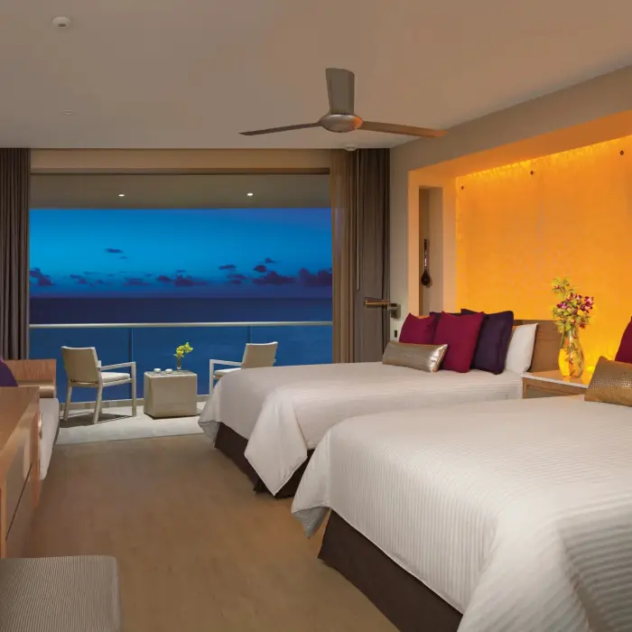Oceanfront junior suite with double beds, warm lighting, and balcony views.