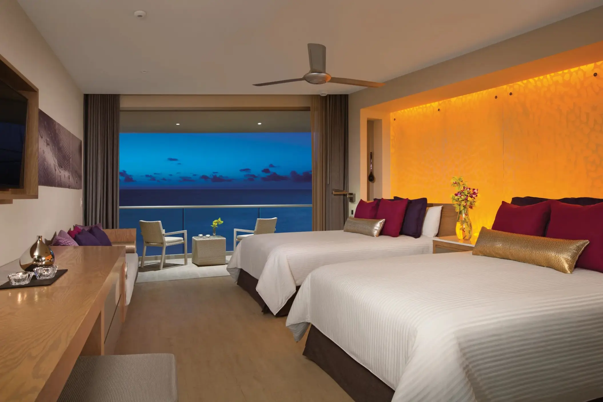 Oceanfront junior suite with double beds, warm lighting, and balcony views.