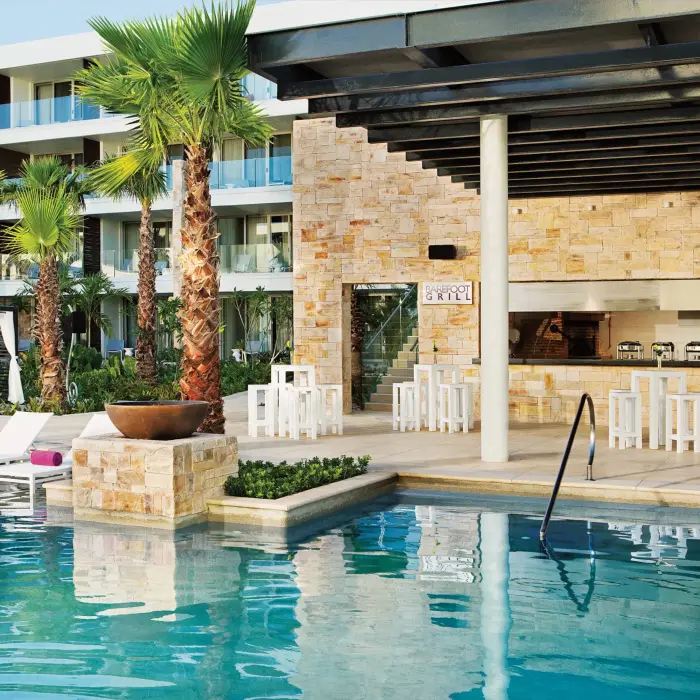 Poolside view of Barefoot Grill restaurant with outdoor seating and tropical landscaping.