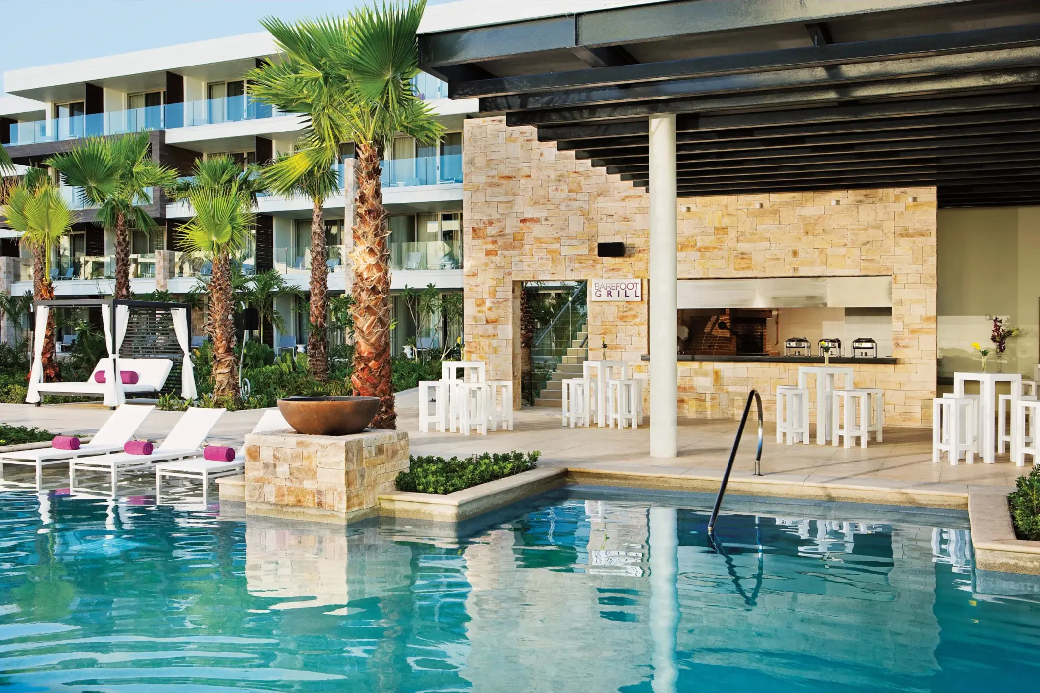 Poolside view of Barefoot Grill restaurant with outdoor seating and tropical landscaping.