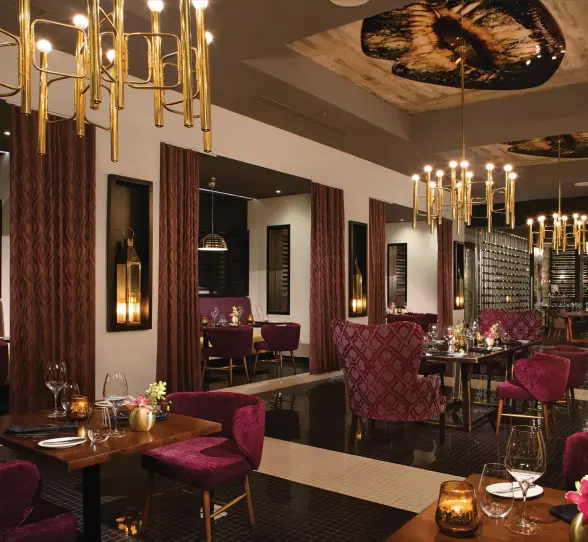 Elegant interior of Coquette restaurant featuring gold chandeliers and plush velvet seating.