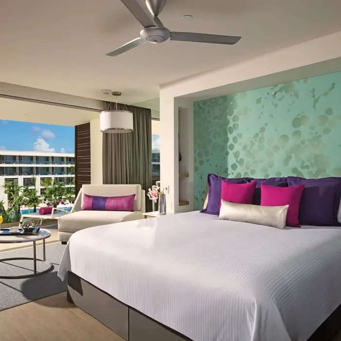 Spacious junior suite with ocean view balcony, king bed, and vibrant decor at Breathless Riviera Cancun.