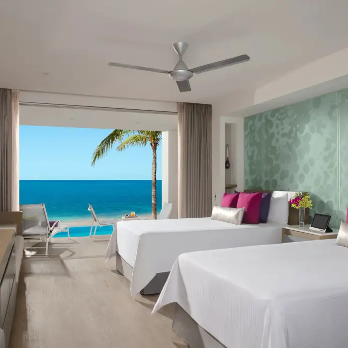 Junior suite with two double beds and oceanfront views, featuring private balcony and tropical design.