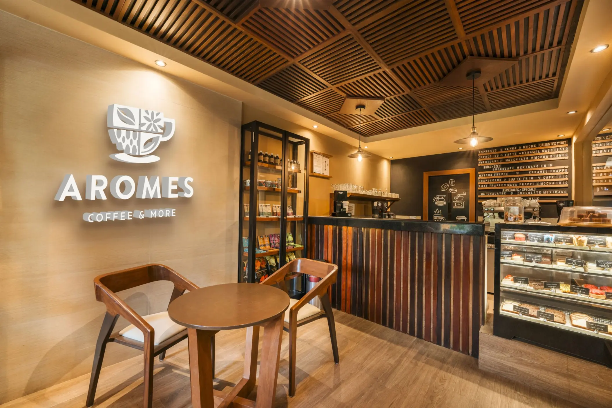 The inviting interior of Aromes Coffee & More cafe at Catalonia Playa Maroma, with warm lighting, wooden accents, and pastries on display.