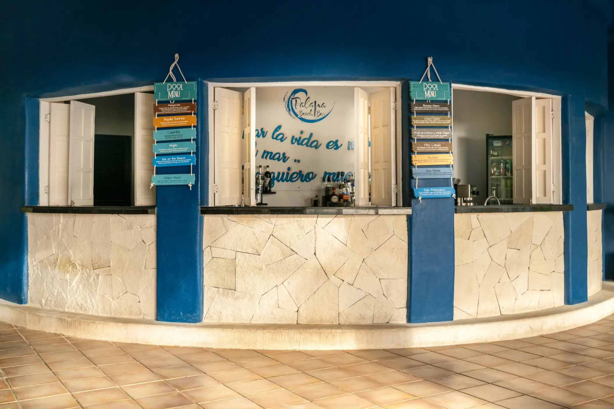 blue and white outdoor bar at Catalonia Playa Maroma with a curved counter and signs for Pool Menu, suggesting a refreshing spot.