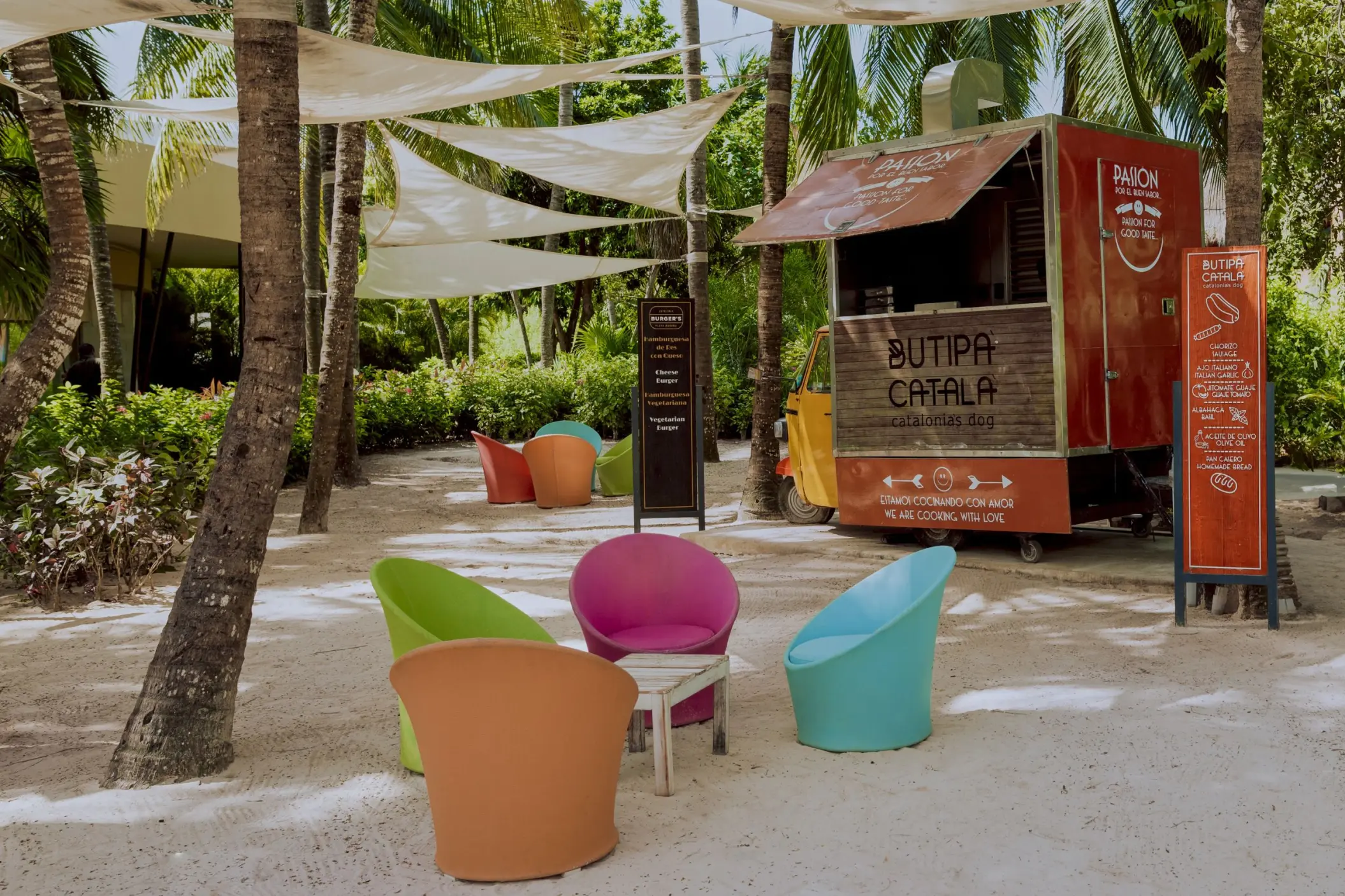 A food truck on a sandy area at Catalonia Playa Maroma beach, surrounded by bright chairs and palm trees.