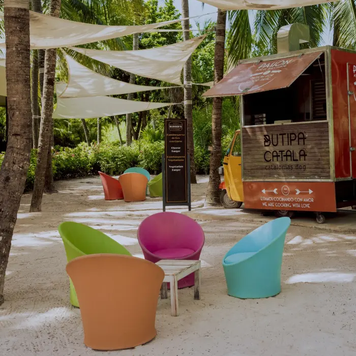 A food truck on a sandy area at Catalonia Playa Maroma beach, surrounded by bright chairs and palm trees.