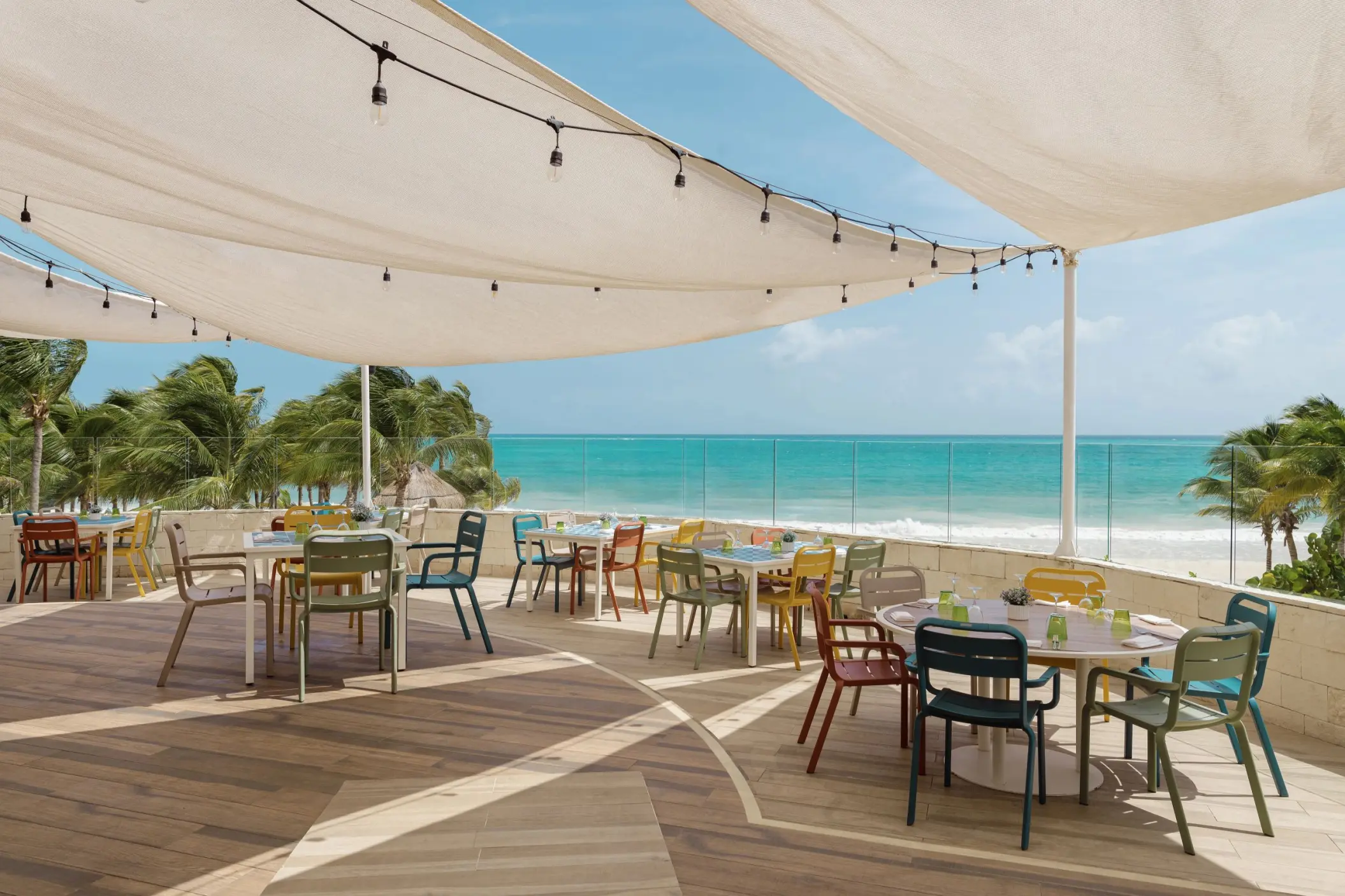 open-air ocean view restaurant at Catalonia Playa Maroma with a canvas shade, colorful tables and chairs, overlooking the turquoise sea.