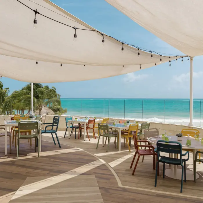 open-air ocean view restaurant at Catalonia Playa Maroma with a canvas shade, colorful tables and chairs, overlooking the turquoise sea.