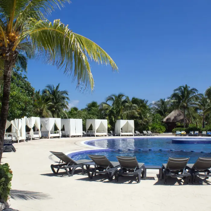 A serene resort pool at Catalonia Playa Maroma with numerous sun loungers and white cabanas under a clear blue sky.